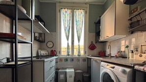 Une petite cuisine équipée d’un lave-linge, d’un évier et d’une fenêtre avec des rideaux.