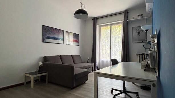 Un salon moderne comprenant un canapé, une petite table, un bureau et un luminaire suspendu au plafond.