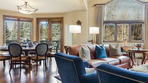 Ein geräumiges Wohnzimmer mit großem Fenster, einem Essbereich mit Holztisch und -stühlen sowie einem blauen Ledersofa.