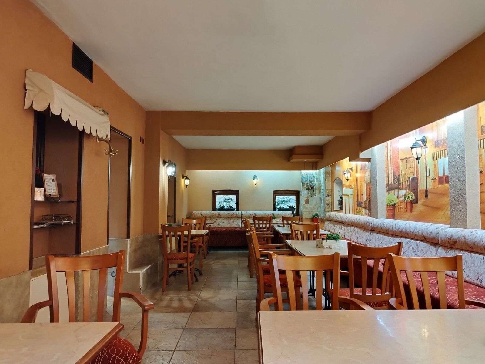 A restaurant with wooden tables and chairs, a long counter, and a mural on the wall.