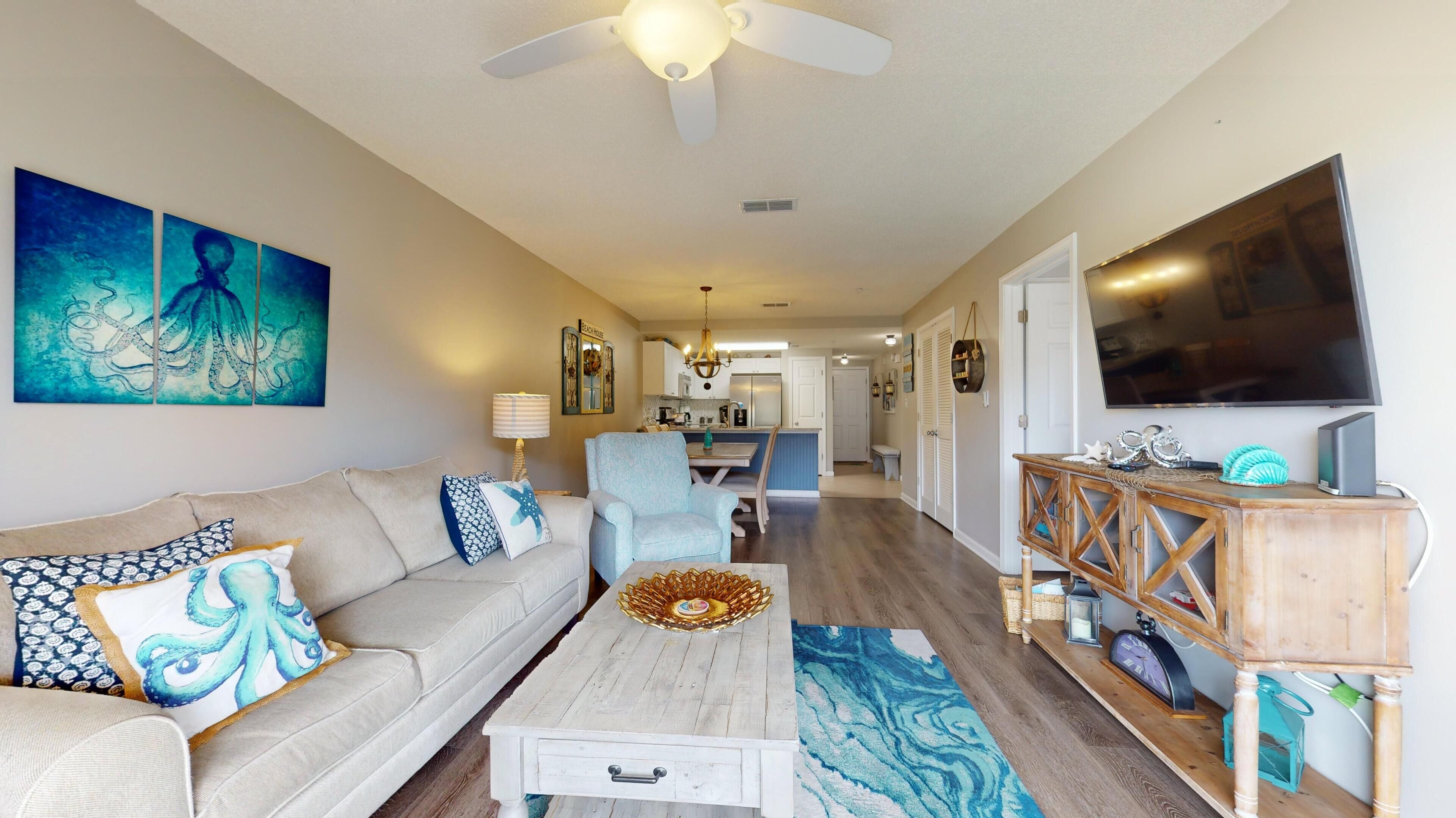 A living room with a sofa, coffee table, and TV stand. There is a dining area with a table and chairs.