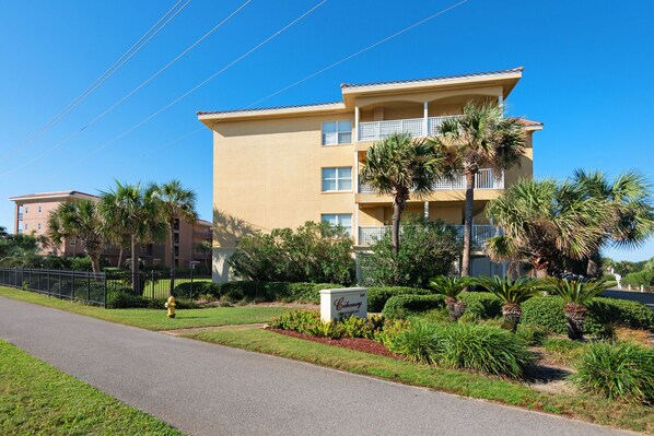 A multi-story hotel with a flat roof, balconies, and a landscaped garden with palm trees.