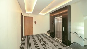 A modern hallway with a wooden door, a black and white striped carpet, and a glass elevator.