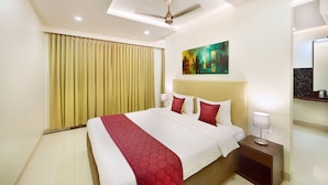 A hotel room with a large bed, a ceiling fan, a painting on the wall, and a nightstand with a lamp.