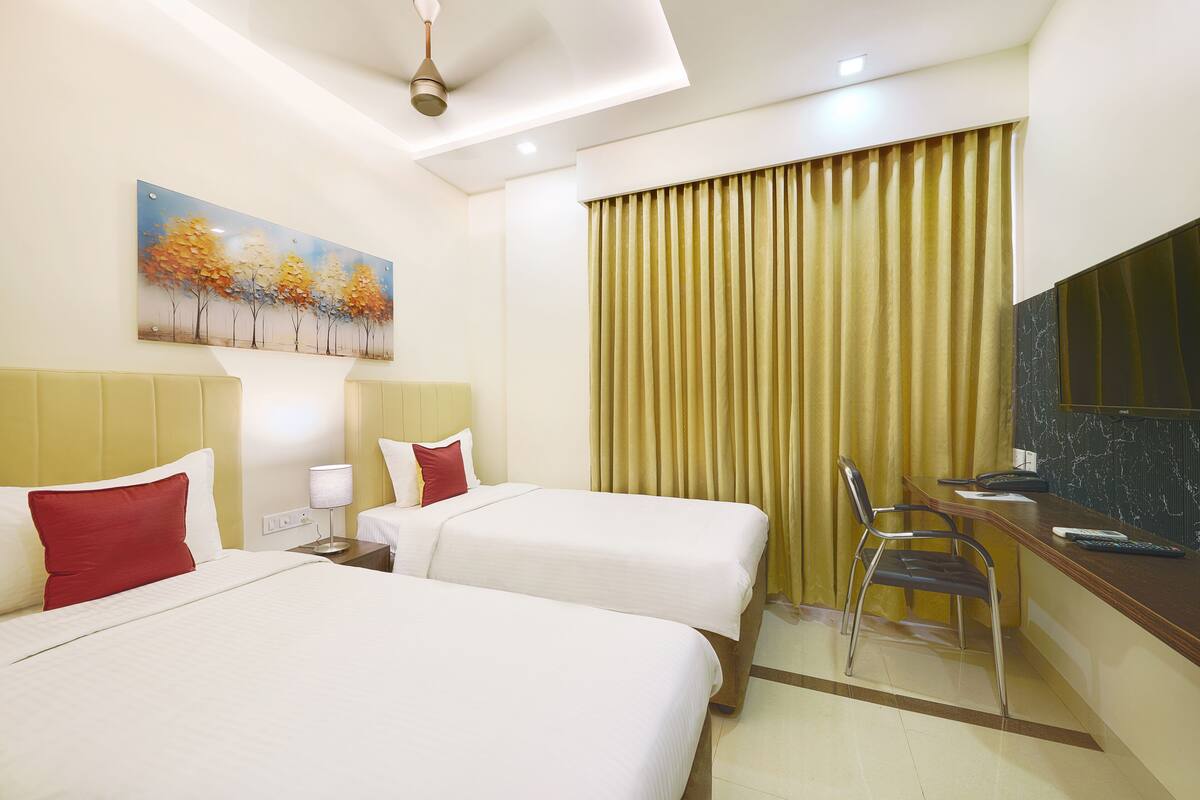 A hotel room with two beds, a desk with a chair, a painting on the wall, and a large window with curtains.