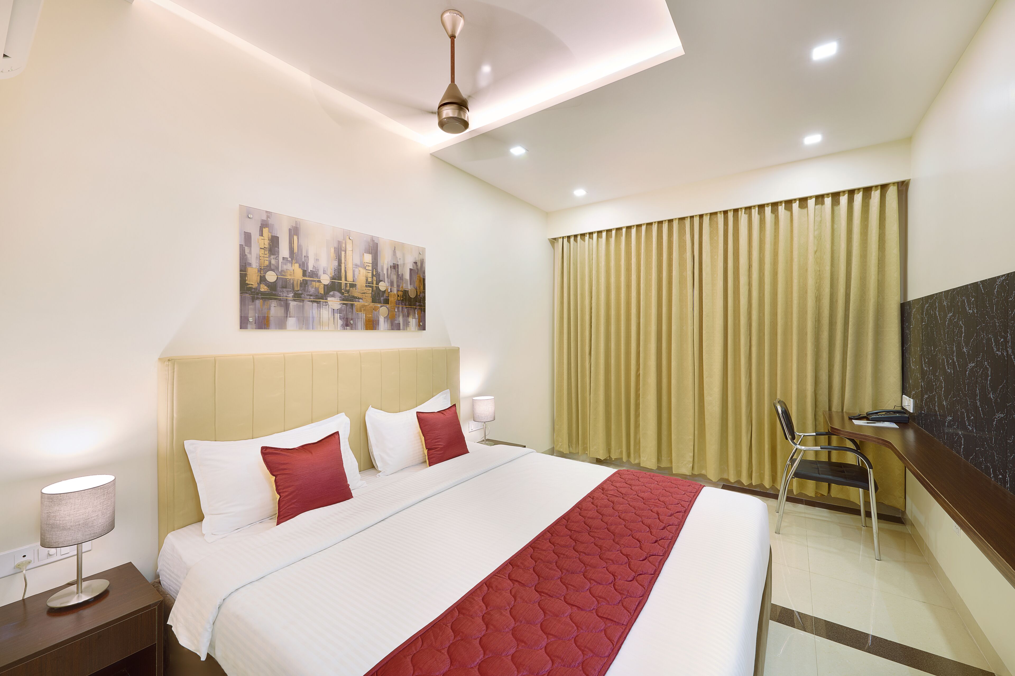 A hotel room with a large bed, a desk, a chair, a painting on the wall, and a window with curtains.