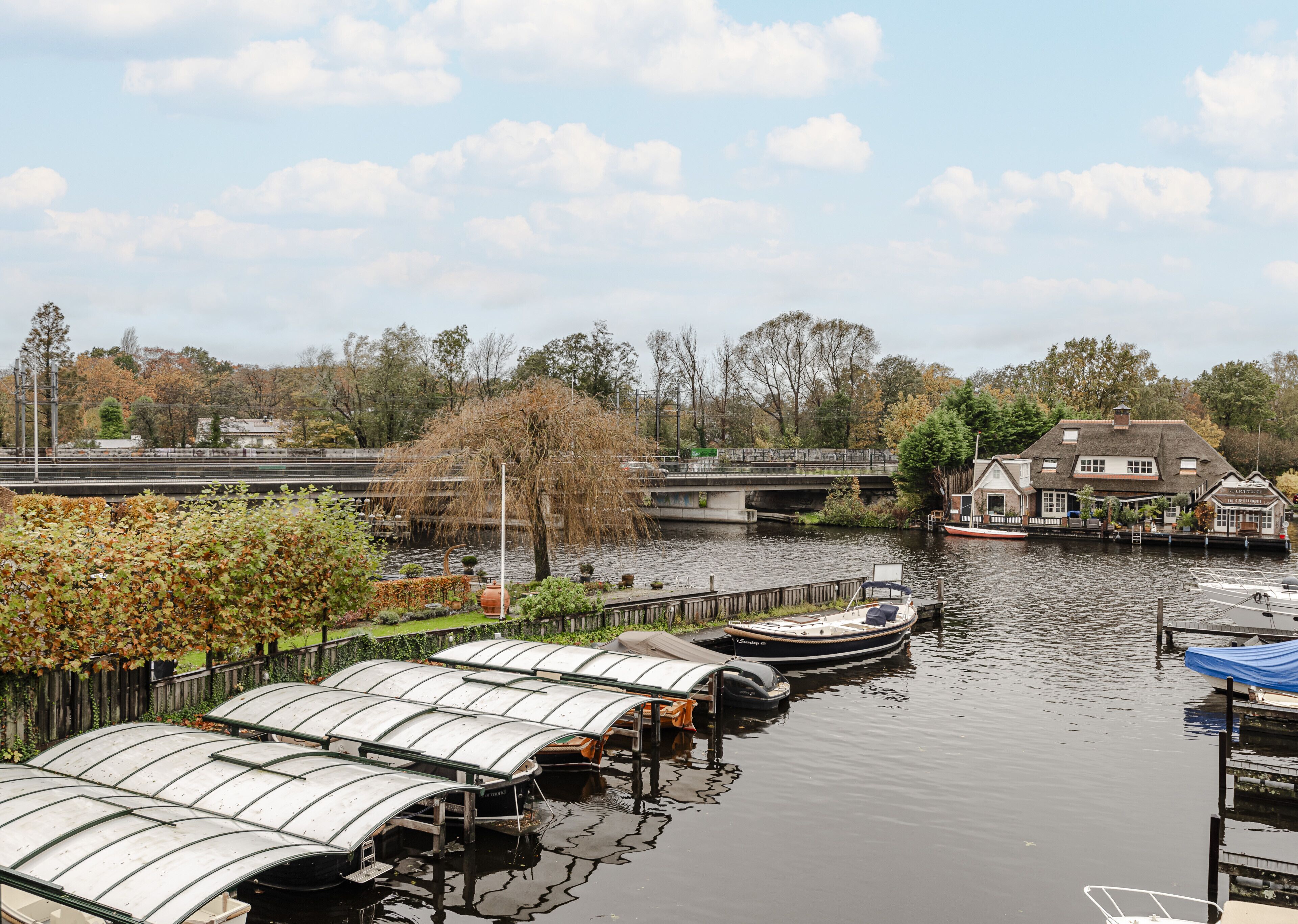 Een steiger aan de rivier met boten, een brug en een gebouw met een bord.