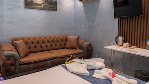 A modern room with a brown tufted sofa, a flat-screen TV, and a painting on the wall. - Stay Suite Hotel (Eyup)