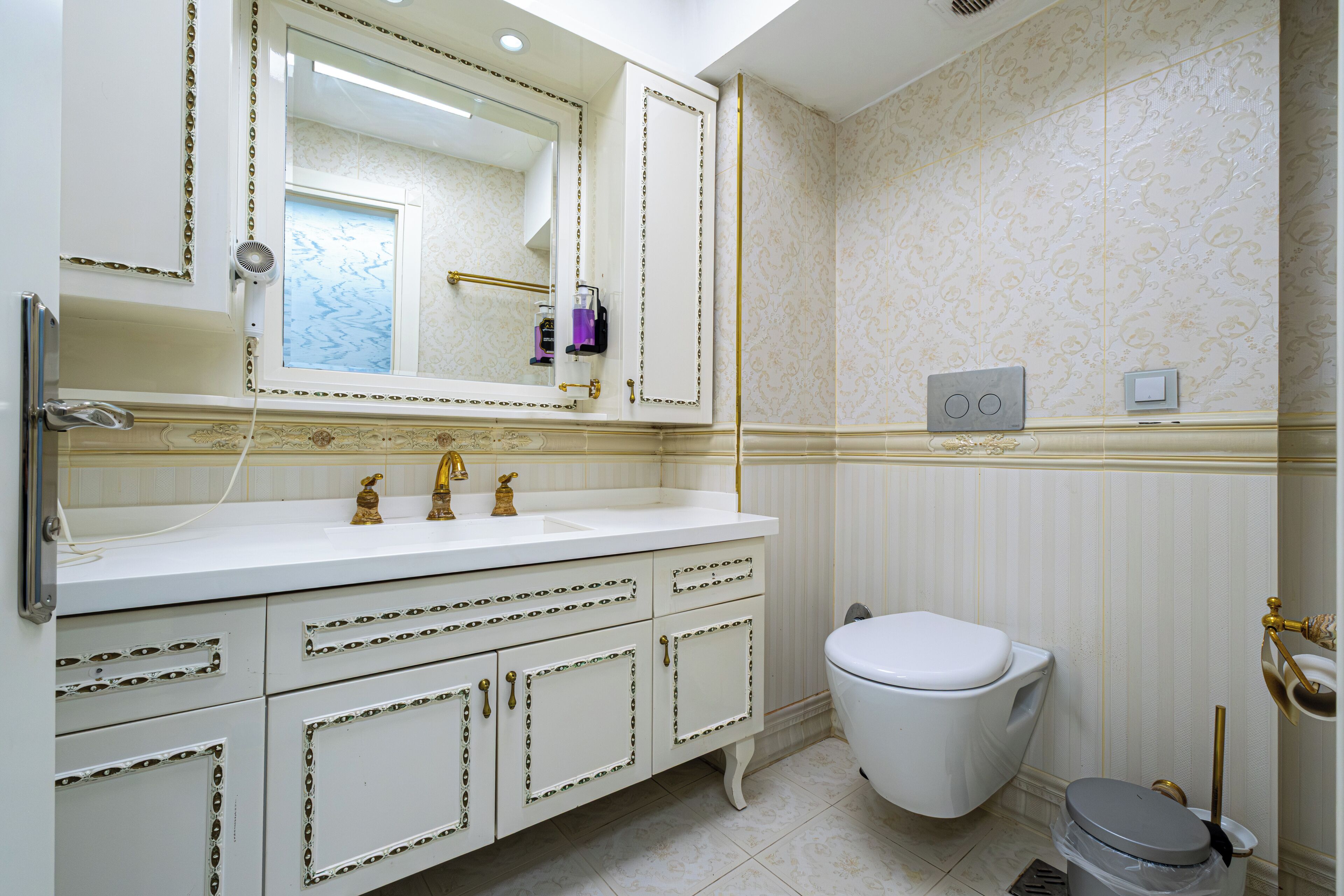 Un baño con lavamanos blanco, detalles dorados y un inodoro.