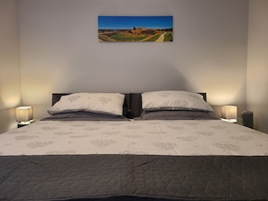 A neatly made bed with patterned bedding, two bedside lamps, and a framed landscape painting on the wall.