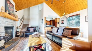 A spacious living room with a fireplace, leather sofa, and a dining area with wooden cabinets. - Mammoth Gateway Village #6 3 Bedroom Condo by RedAwning (Mammoth Lakes)