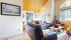 A spacious living room with a black leather sofa, a wooden coffee table, and a dining area with a wooden table and chairs. - Mammoth Gateway Village #6 3 Bedroom Condo by RedAwning (Mammoth Lakes)