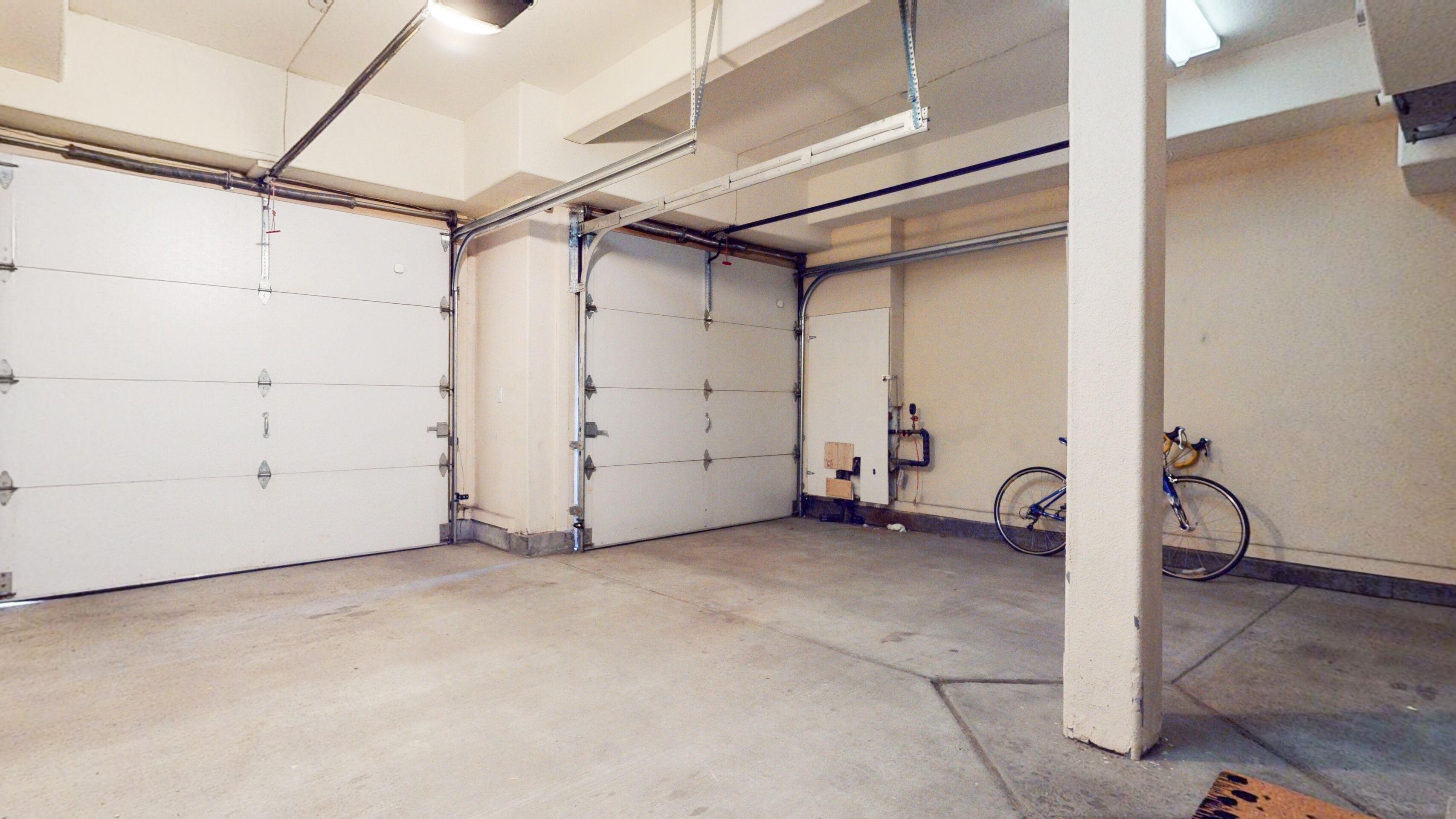 A clean, empty garage with white doors, exposed pipes, and a bicycle leaning against the wall.