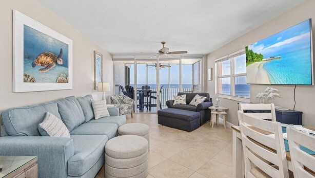 A spacious living room with a large window, a ceiling fan, and a flat-screen TV. - Beach Villas # 506-250 Estero Blvd 2 Bedroom Apts by RedAwning (Fort Myers Beach)