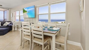 A dining area with a view of the sea, a sofa, and a TV mounted on the wall. - Beach Villas # 506-250 Estero Blvd 2 Bedroom Apts by RedAwning (Fort Myers Beach)
