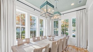 A dining area with a wooden table and wicker chairs, large windows with curtains, and hanging glass chandeliers. - 107 Sunflower Street 5 Bedroom Home by RedAwning (Santa Rosa Beach)