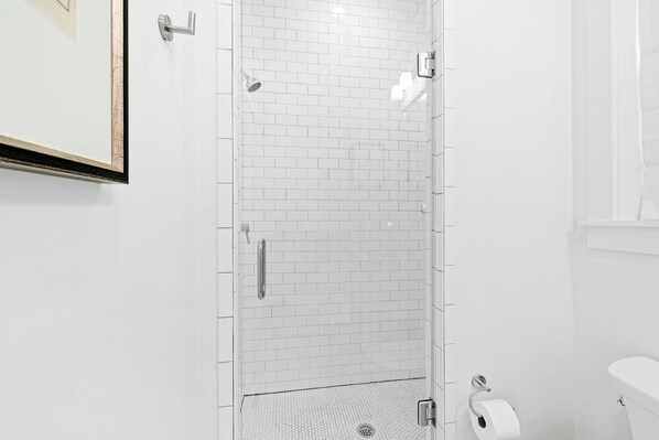 Un baño moderno con azulejos blancos tipo metro, un box de ducha de vidrio, un inodoro y un cuadro en la pared.