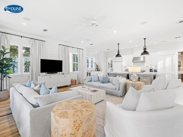 Relax in this inviting living area with a large L-shaped sofa, flat-screen TV, and modern kitchen in the background.