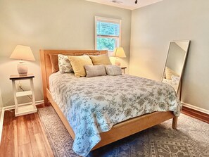 A bedroom with a bed, two bedside tables, a nightstand, a window, and a mirror.