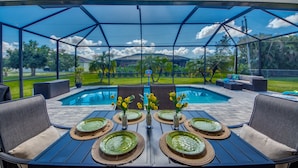Une terrasse extérieure avec une piscine, un espace salon couvert et une table dressée pour les repas.