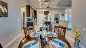 Un coin repas avec une table ronde dressée pour quatre personnes, un lustre et un vase rempli de fleurs.