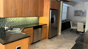 A modern kitchen with wooden cabinets, a stainless steel refrigerator, a dishwasher, and a ceiling fan. - Stunning Waterfront 2-bdrm condo with Executive Office & Boat Lift (Punta Gorda)