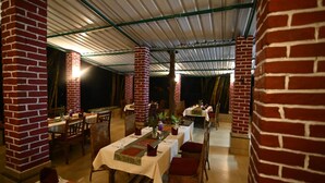 An indoor dining area with brick pillars, tables set with white tablecloths, and chairs. - Rosewood Resort (Bichhiya)