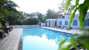 A swimming pool with lounge chairs and a covered area, surrounded by a white wall with blue floral designs. - Rosewood Resort (Bichhiya)