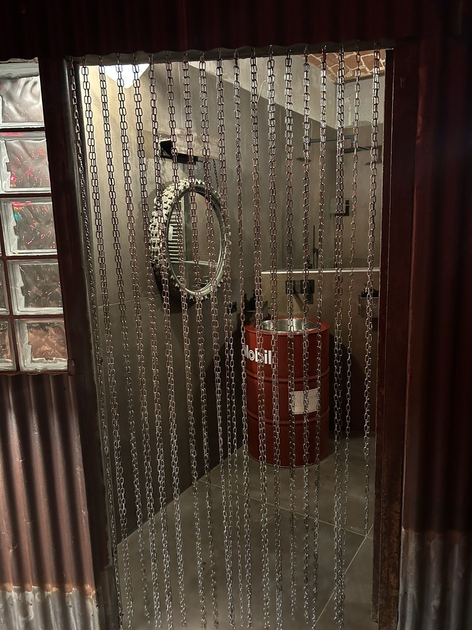 A room with a chain-link curtain, a circular mirror, and a red barrel.