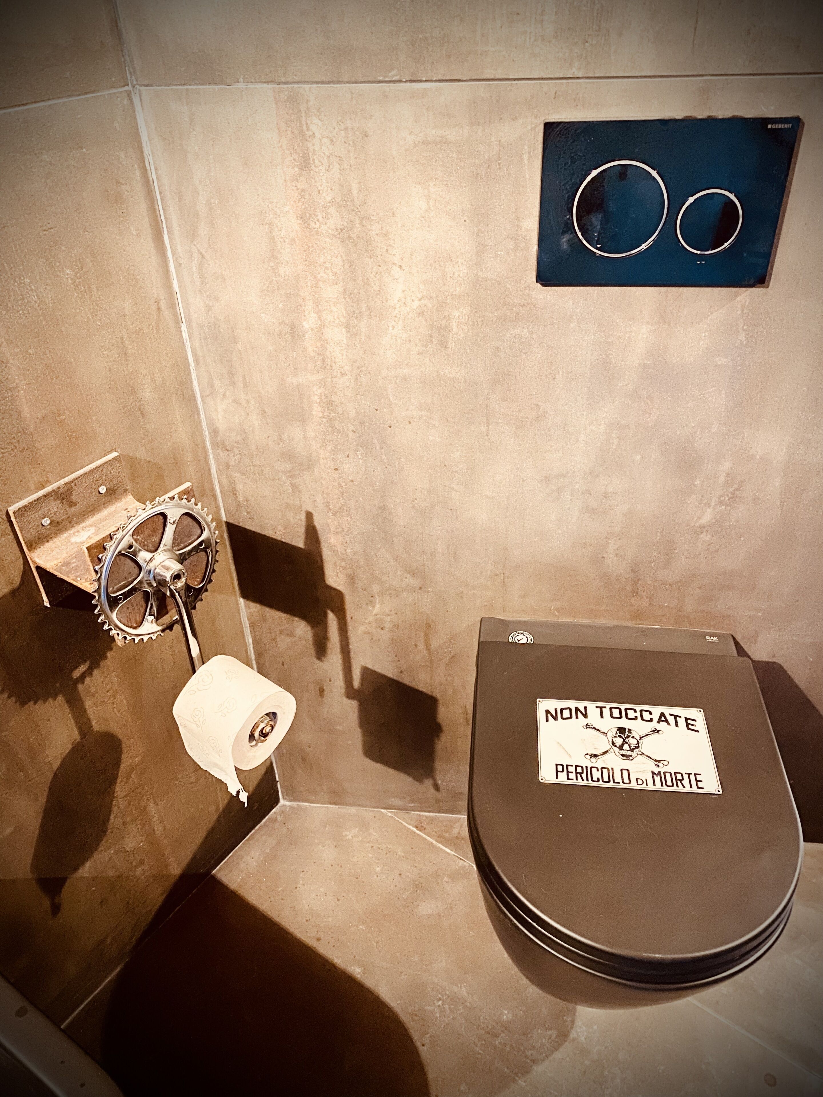 A bathroom with a toilet, a hand dryer, and a sign warning 'NON TOCCATE PERICOLO DI MORTE'.
