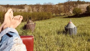 Una persona relaxant-se en un prat amb un cel blau clar, una cadira vermella i dues cistelles de vímet.