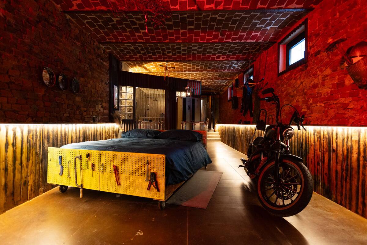 A room with a bed, a motorcycle, and a brick wall.