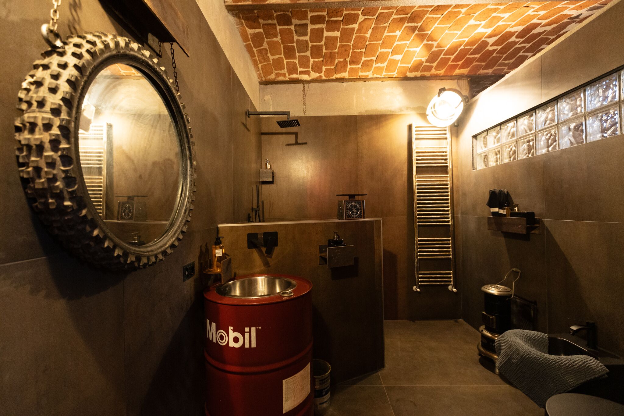 Un baño con un espejo grande, un barril rojo, un perchero y una zona de ducha.