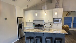 A modern kitchen with white cabinets, a granite countertop, stainless steel appliances, and a bar stool area.