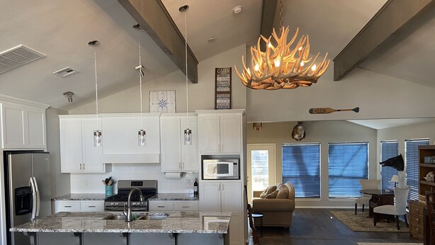 A spacious kitchen with white cabinets, a central island with stools, a microwave, and a stainless steel refrigerator.