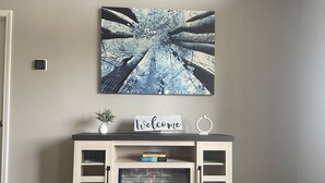 A fireplace with a 'Welcome' sign, a framed artwork above it, and a small plant on the mantel.