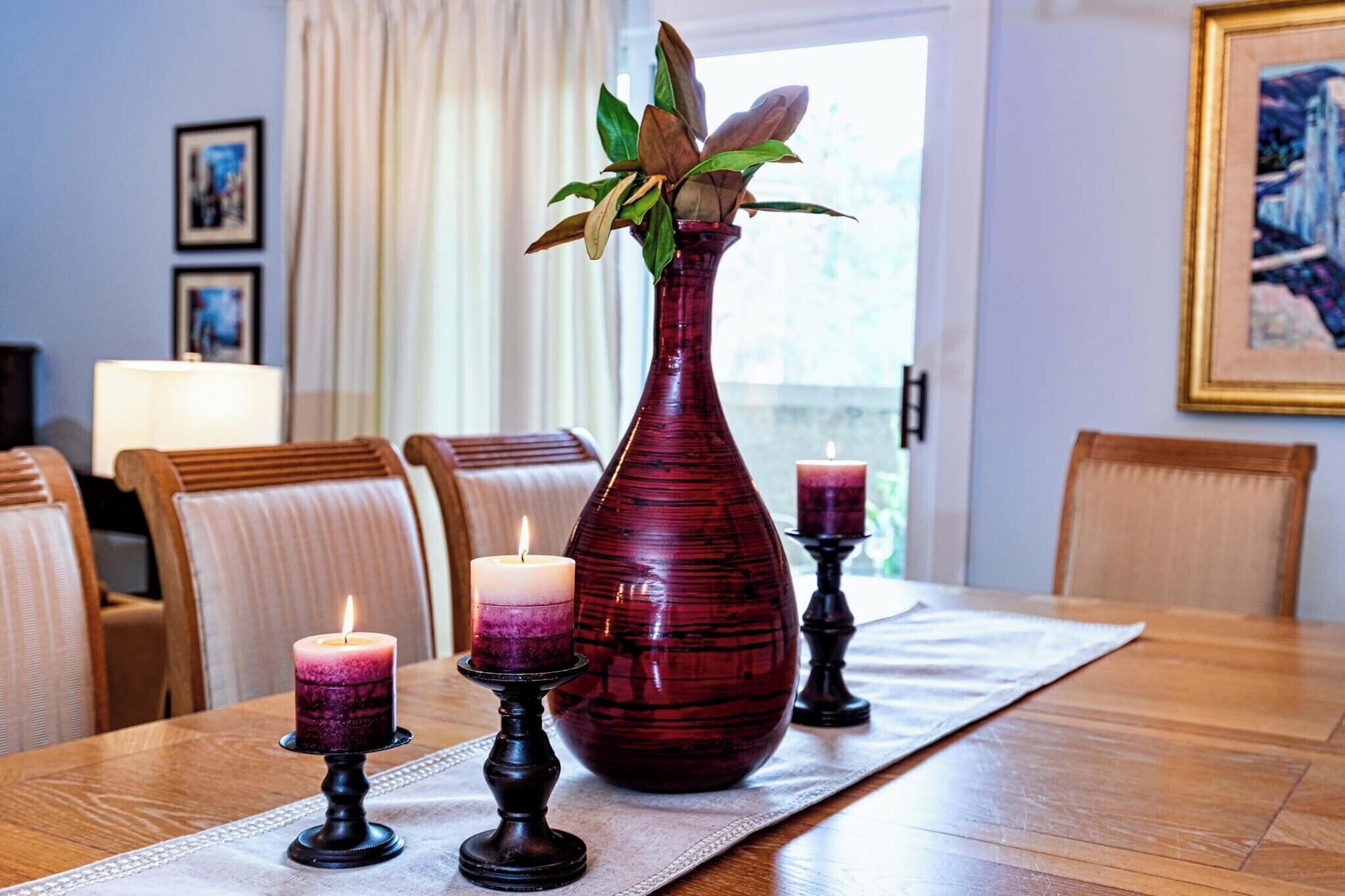 Una mesa de comedor con un florero rojo, dos velas y un mantel individual.
