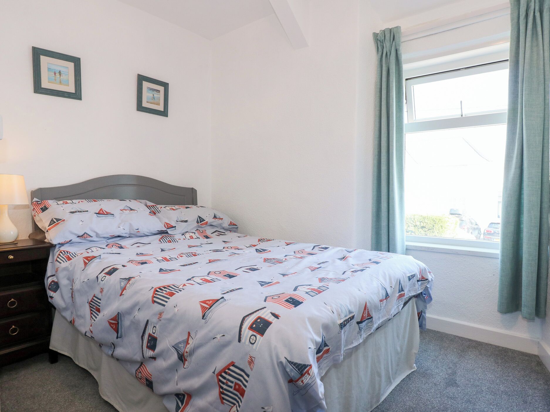 Una camera da letto con un letto, un comodino, una lampada, due quadri appesi al muro e una finestra con tende.