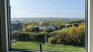 Une vue depuis une fenêtre donnant sur un paysage rural, avec des maisons, des haies et un ciel dégagé.