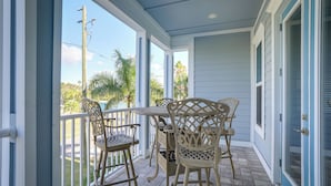 A covered patio with a table and chairs, overlooking a view of palm trees and a clear sky. - Steps to Shore: Modern Redington Beach Townhome (Redington Beach)
