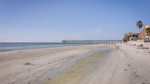 A beach with a pier extending into the water, sandy shore, and buildings in the background. - Steps to Shore: Modern Redington Beach Townhome (Redington Beach)