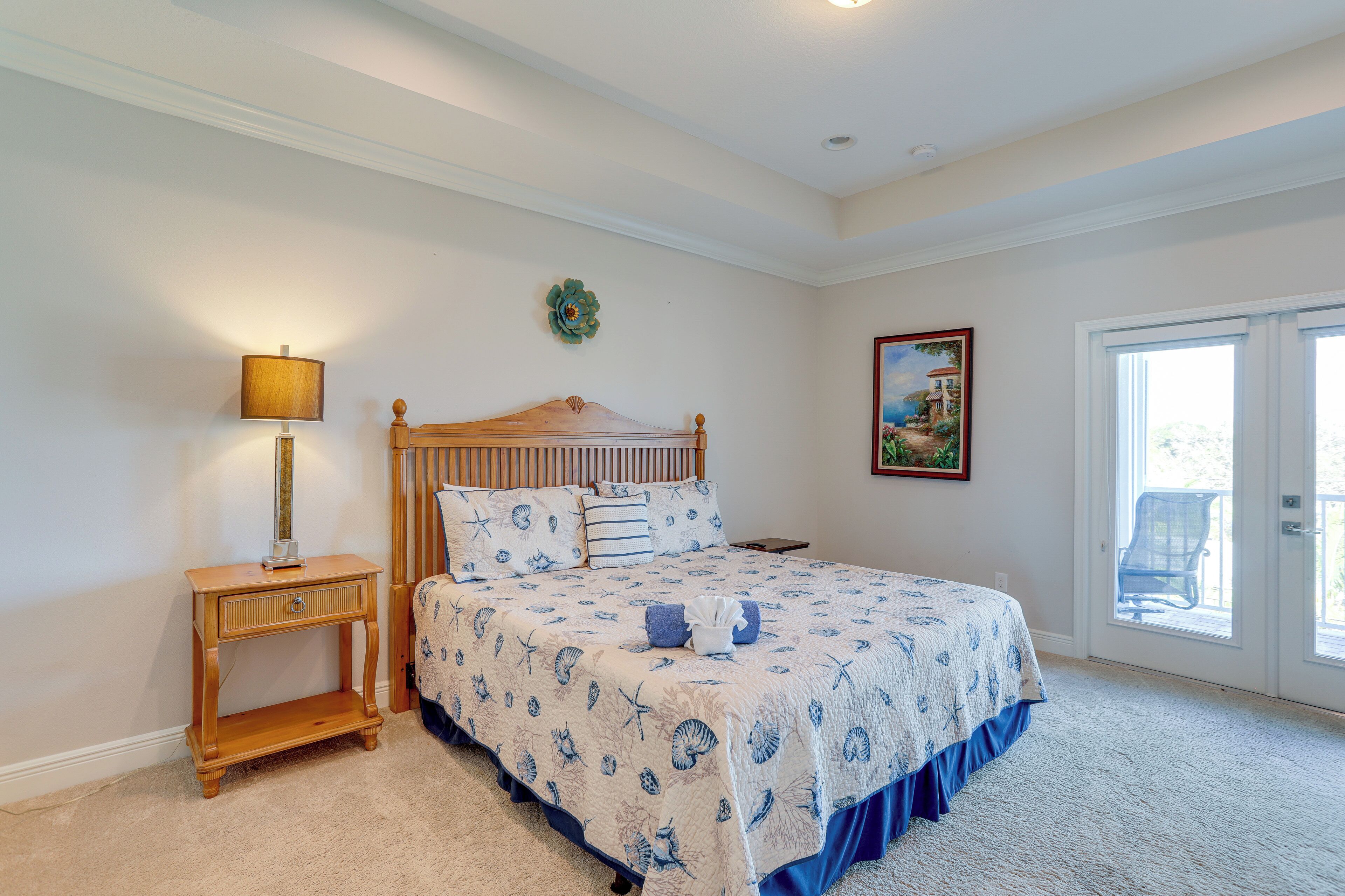 A bedroom with a bed, a nightstand, a lamp, a framed picture, and a door leading to a balcony.