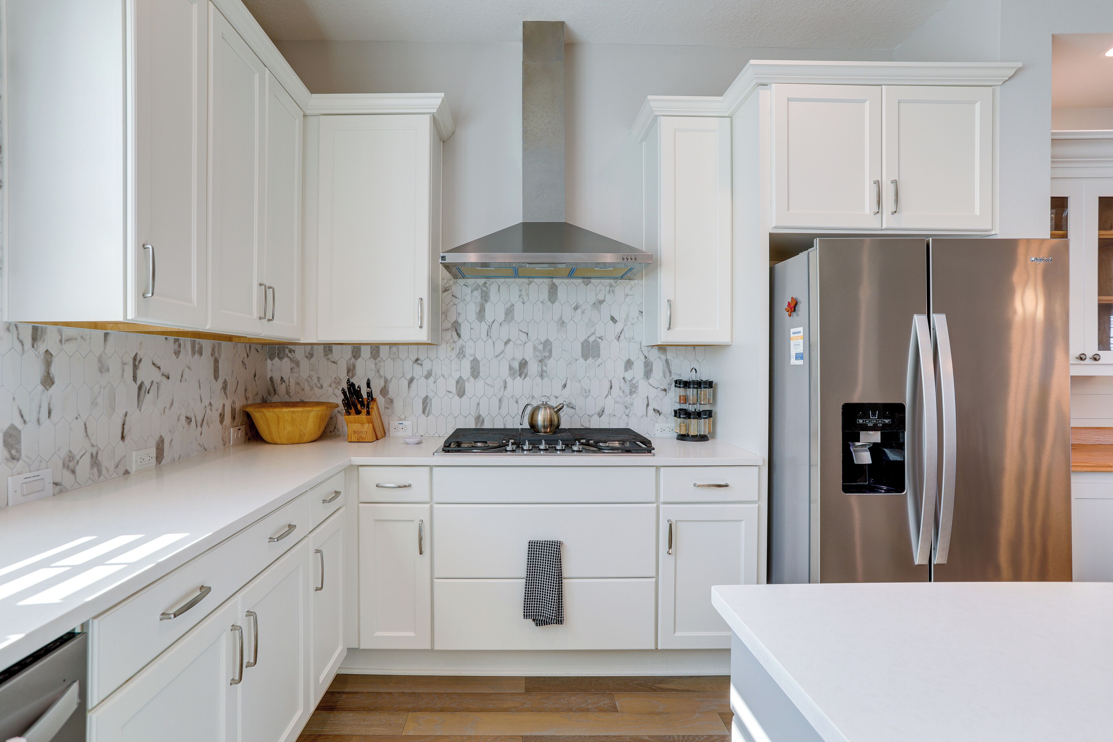 Una cocina moderna con armarios blancos, un refrigerador de acero inoxidable y una estufa a gas con campana extractora.