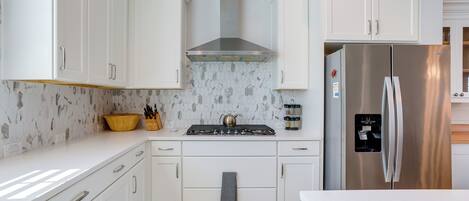 Una cocina moderna con armarios blancos, un refrigerador de acero inoxidable y una estufa a gas con campana extractora.