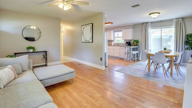 A modern living room with a sectional sofa, a dining area with a wooden table and chairs, and a kitchen in the background.