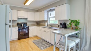 A modern kitchen with white cabinets, a stainless steel oven, a granite countertop, and a wooden dining table with two bar stools.