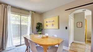 A dining area with a wooden table, four chairs, a potted plant, and a framed picture on the wall.