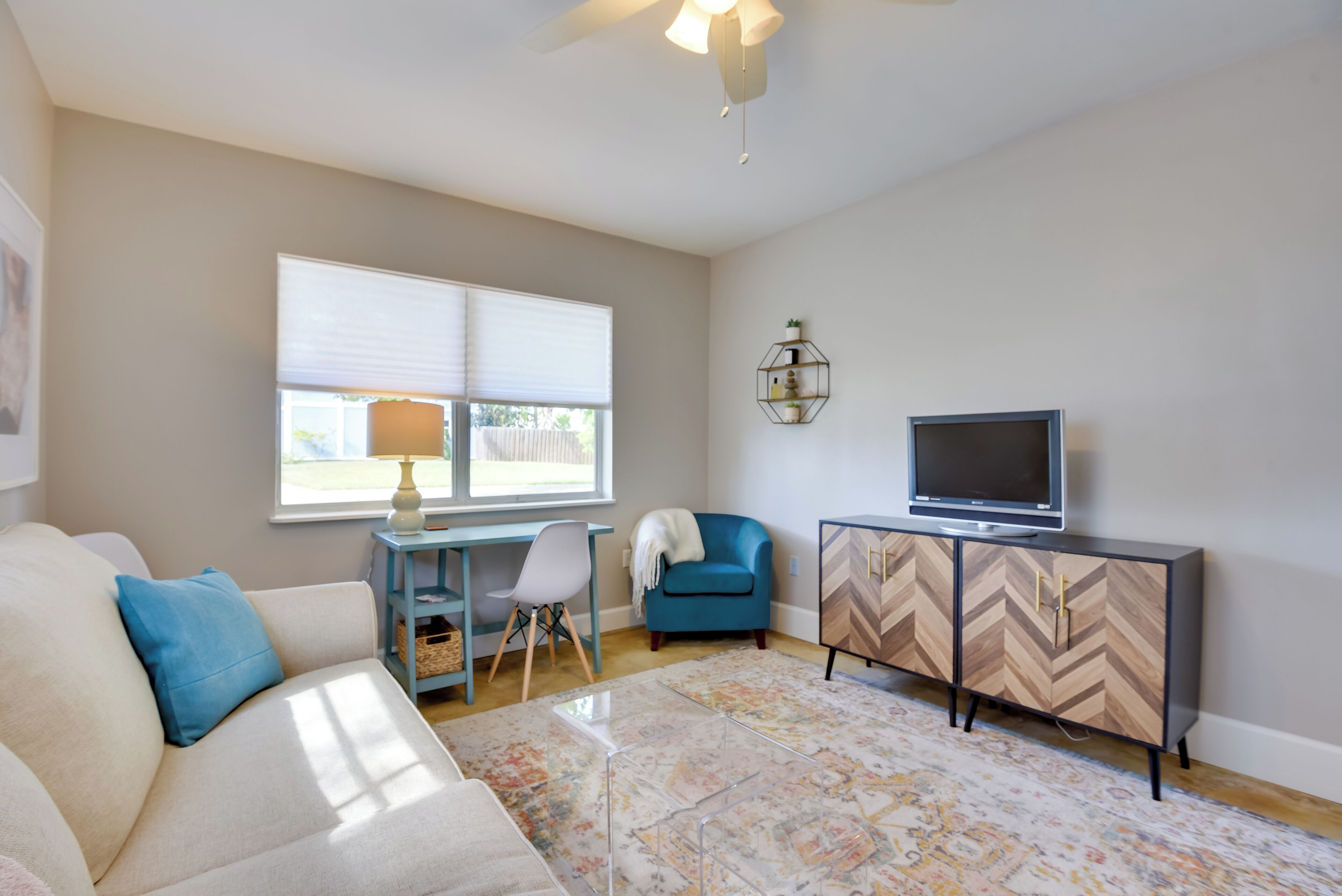 A living room with a sofa, a desk, a chair, a television, and a cabinet.