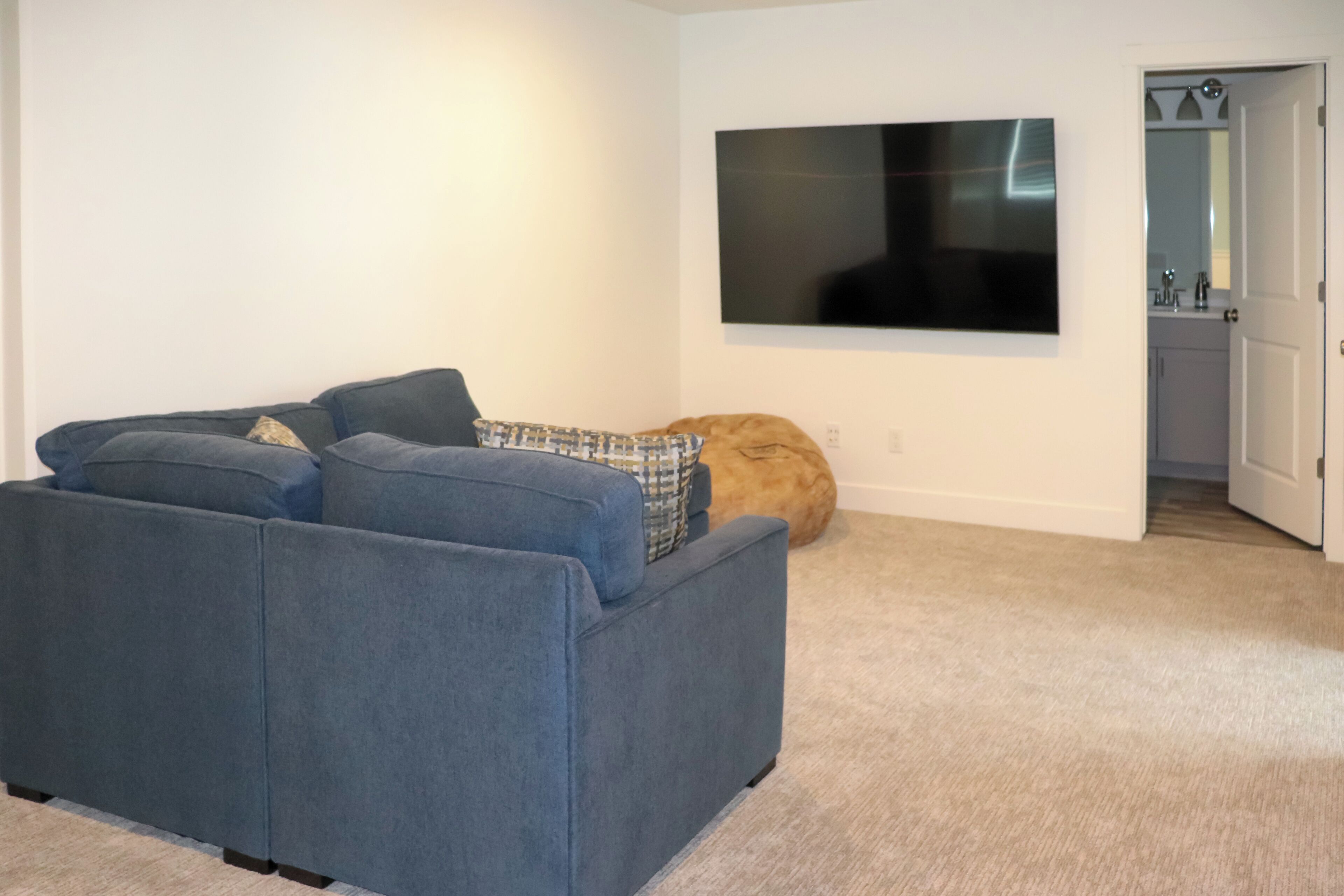 Ein Wohnzimmer mit einem blauen Sofa, einem an der Wand montierten Fernseher und einer Katze, die auf dem Boden liegt.