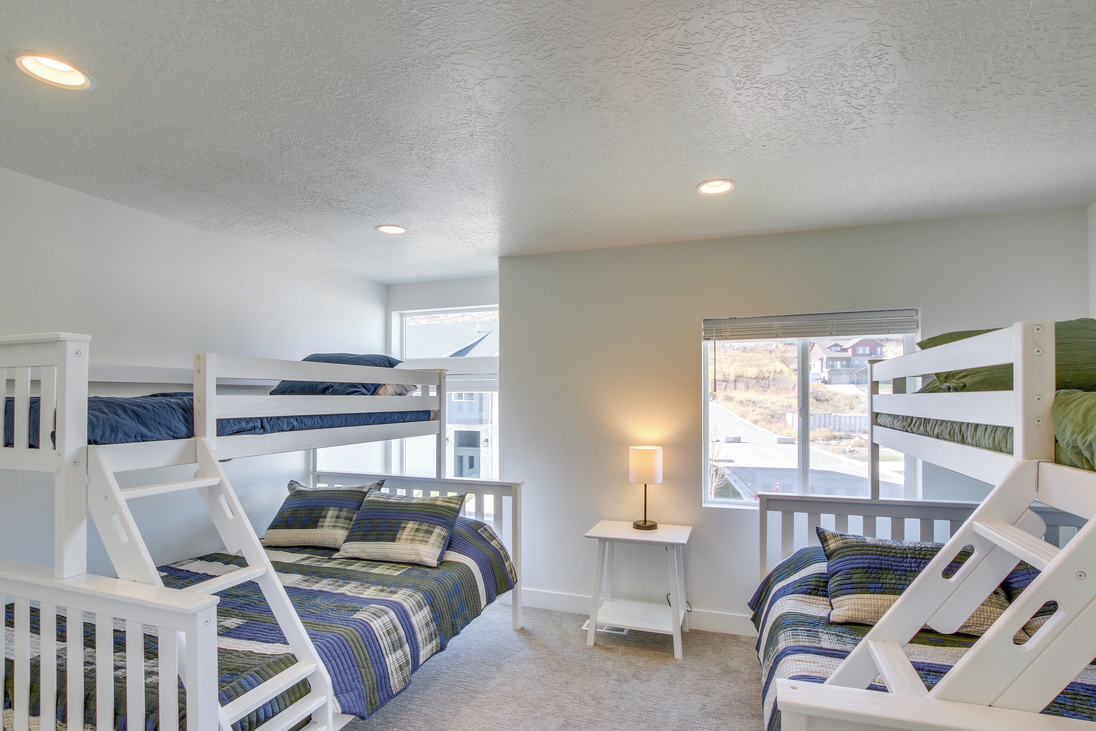A room with bunk beds, a small table with a lamp, and a window with a view of the outside.